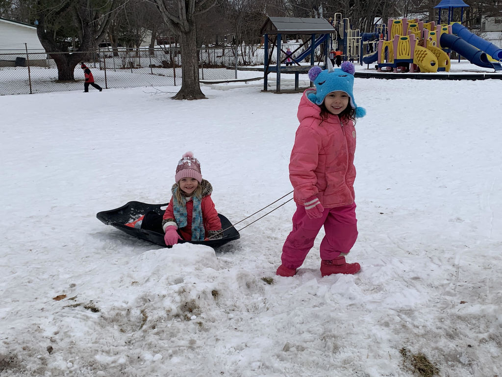 Girl pulling another girl on a sled in the snow
