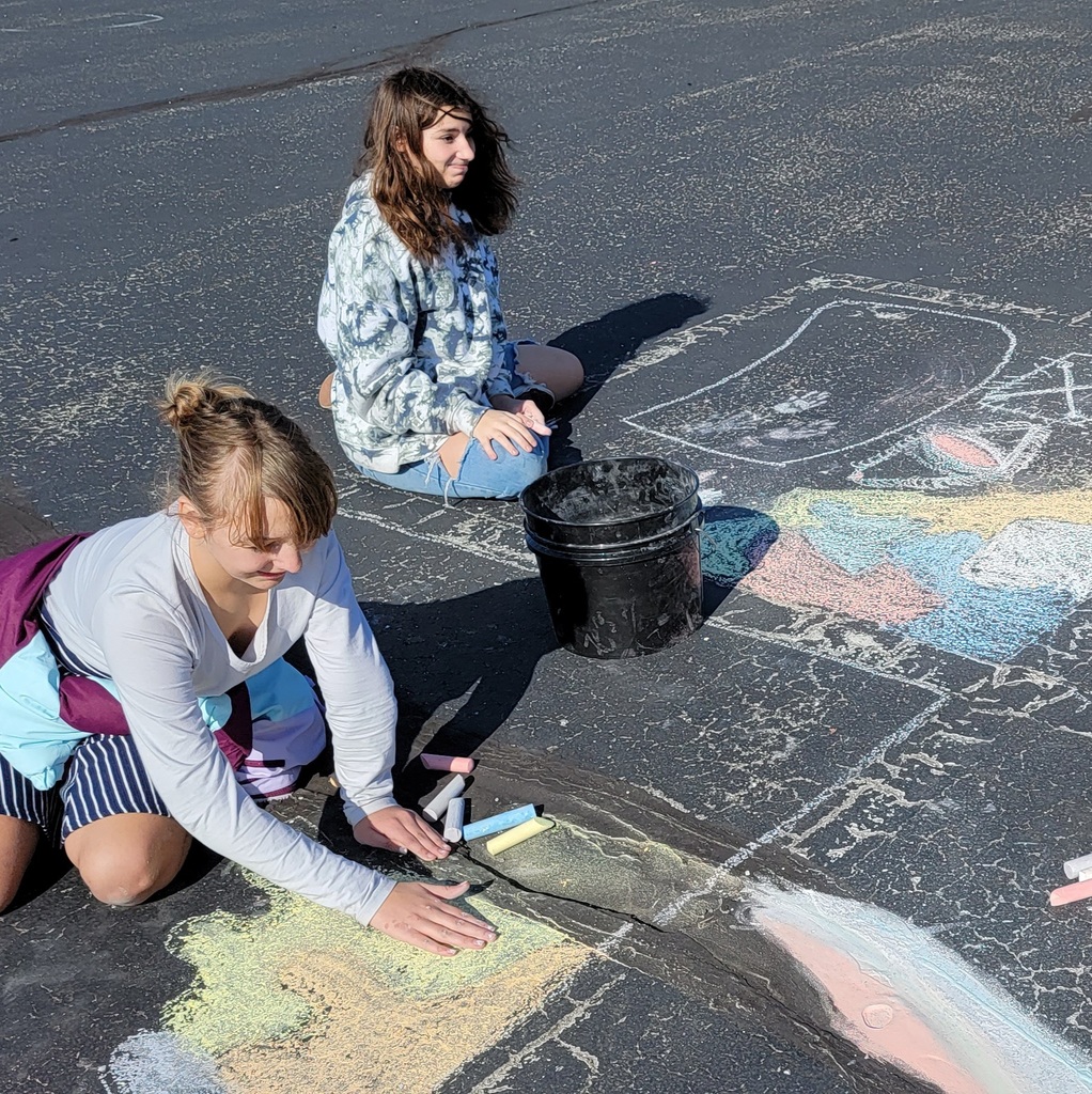 two students using chalk on the playground